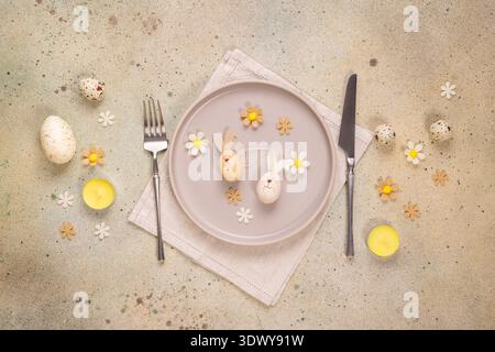 Easter table setting showing decorated plate with wooden bunny eggs, cutlery, candles, and decorative flowers, creating a festive atmosphere for sprin Stock Photo
