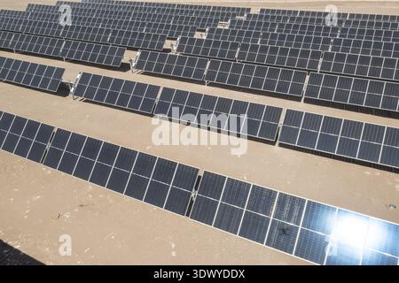High-angle drone shot of solar photovoltaic arrays in a desert landscape, part of a hybrid wind-solar power facility. Stock Photo