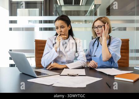 Medical professionals experiencing stress and anxiety while reviewing critical patient information on a laptop, coping with challenging decisions and potential burnout in a healthcare environment Stock Photo