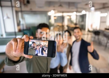 Diverse business team displayed on smartphone screen while taking selfie Stock Photo