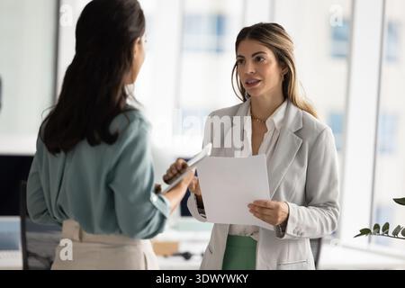 Two businesswomen colleagues team members discussing paperwork at modern office Stock Photo