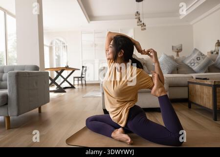 Smiling young woman practicing complex seated yoga stretch indoors Stock Photo