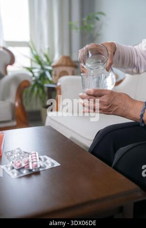 The elderly woman pouring water into the glass is taking her medicine. Stock Photo