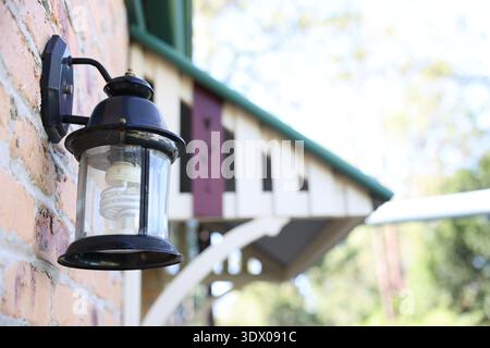Outdoor wall-mounted lantern light on a brick wall with blurred architectural background. Stock Photo