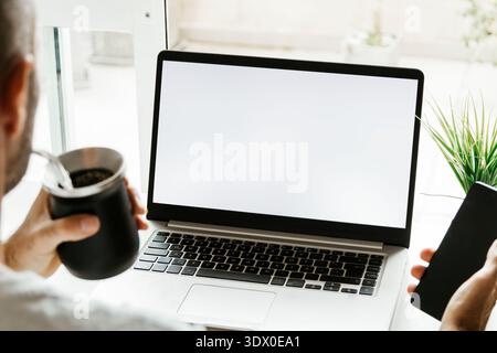 Man hands using laptop with empty screen. Blank white screen. Argentinian user using a computer while drinking yerba mate. Photo ready for mockup. Stock Photo