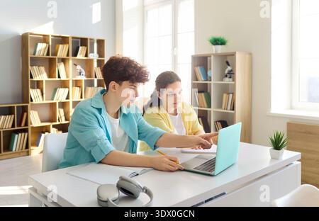 Teen students pointing at laptop screen in library classroom during group study Stock Photo