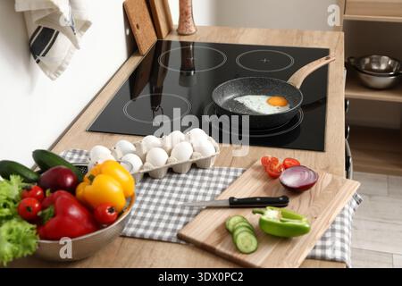 Fresh vegetables and frying pan of chicken egg on stove in kitchen Stock Photo