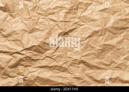 A crumpled and flattened brown craft paper sheet, showcasing a dense network of creases, ridges, and organic textures that create a dynamic play of light and shadow. Stock Photo