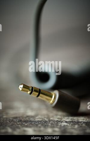 Macro shot of a gold-plated stereo mini-plug connector with a blurred cable on a textured surface Stock Photo