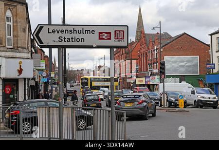 Traffic and vehicle congestion on the A6 Stockport Road in Levenshulme, south Manchester, beside a sign pointing to Levenshulme Station. Stock Photo