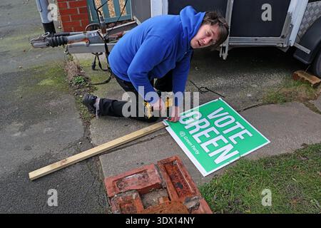 Green Party volunteer installing a “Vote Green” garden stake board outside a supporter’s home in Denton, Greater Manchester, England, UK. Stock Photo