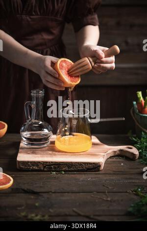 Woman Squeezing Fresh Grapefruit Juice with Wooden Reamer into Glass Pitcher Stock Photo