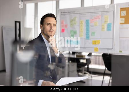 Thoughtful middle adult businessman holding report in office looking away Stock Photo
