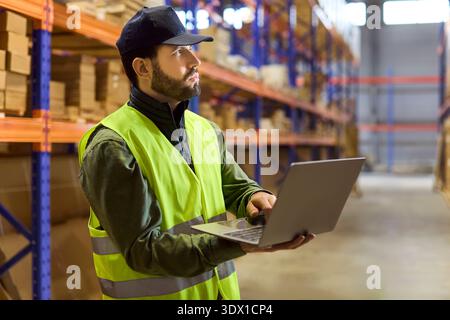 Logistics associate using laptop for inventory audit on warehouse shelves stock Stock Photo