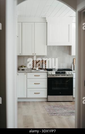 Bright modern kitchen interior featuring white cabinetry, built in oven, marble style backsplash, and clean minimalist design in a contemporary home. Stock Photo