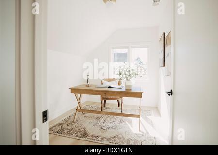 Bright minimalist home office interior with wooden desk, chair and natural window light in a modern residential home. Stock Photo