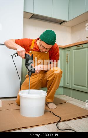 Man mixing mortar with an electric drill in a bucket, preparing plaster or tile adhesive for kitchen renovation and home repair, focused on diy construction work Stock Photo