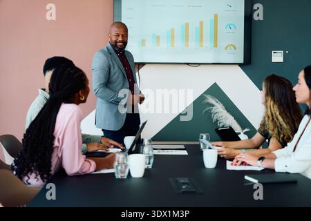 Confident mature businessman presenting growth analytics on screen in boardroom at office during daytime Stock Photo
