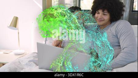 Watching two men, one wearing gray shirt, leaning on bed with laptop showing teal-green overlay Stock Photo