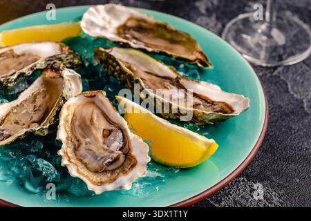 Opened fresh oysters on a blue plate, served with lemon and ice. Stock Photo