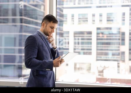 Focused businessman thoughtfully analyzing data or read information on tablet Stock Photo