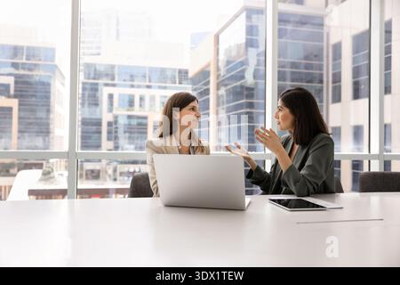 Two professional women having discussion in modern glass-walled boardroom Stock Photo