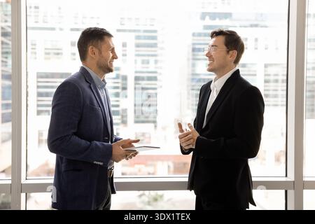 Two businessmen lead conversation standing near window with cityscape view Stock Photo