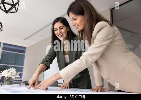 Women engaged in strategic planning, collaborative discussion over printed charts Stock Photo