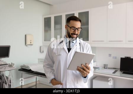 Smiling confident young doctor using digital tablet in examination room Stock Photo