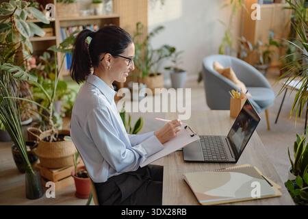 Young Adult Caucasian Woman Taking Notes during Online Psychology Consultation Stock Photo