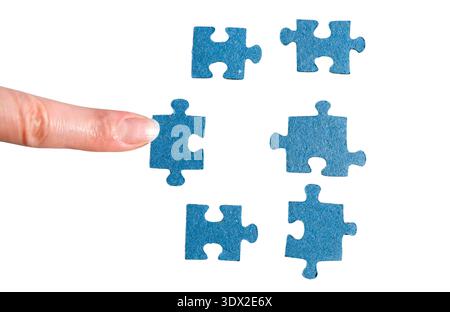 A finger adds a blue jigsaw piece. A hand holding a puzzle piece. Stock Photo