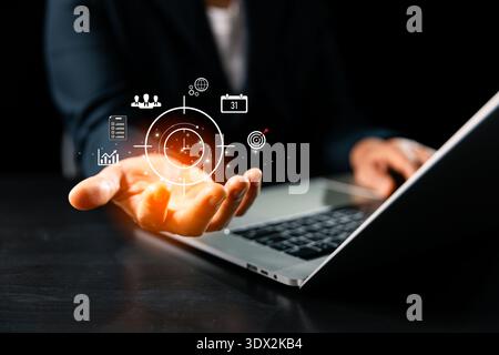 Business professional presenting holographic productivity target and clock over laptop, highlighting time management, task planning, KPI tracking, tea Stock Photo