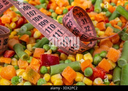 Pink measuring tape on frozen chopped vegetables mix, close up , weight  concept Stock Photo