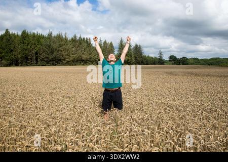 Triumphant mature man with arms raised in the air symbolizing succes and happiness standing in a corn field a summer day Stock Photo