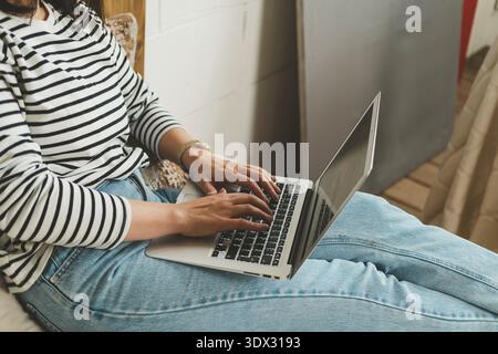Beautiful woman is sitting at home and working on a laptop. Small internet business owner. Distant work. A woman makes purchases in an online store. Womens hands are typing on a laptop, close-up. || Model released Stock Photo