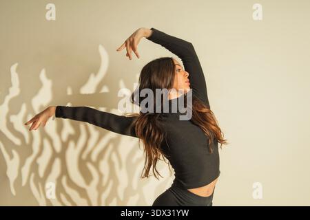 Young woman posing gracefully against a wall with striking light and shadow patterns Stock Photo