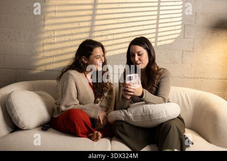 Happy young women friends relaxing on couch sharing smartphone content Stock Photo