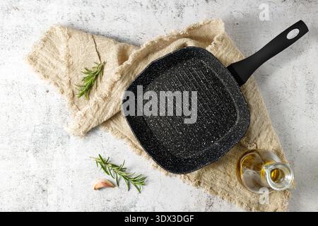 Empty grill pan with olive oil, rosemary and garlic on vintage plate over linen towel. Mockup with space for dish on retro stone table. Stock Photo