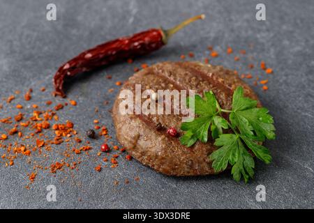 Fresh grilled cutlet patty beef minced meat for burger or dinner dish  closeup with parsley and chilli pepper on dark grey stone background Stock Photo