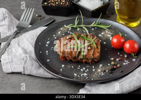 Black Angus Eye of round steak marinated and grilled on black retro plate with rosemary herb,spices and cherry tomatoes on stone table background. Ser Stock Photo