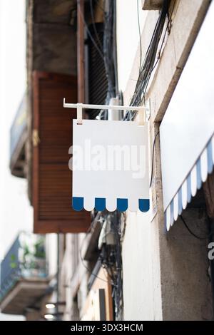 Blank rectangular shop sign blue scalloped edges hanging from a metal bracket Stock Photo