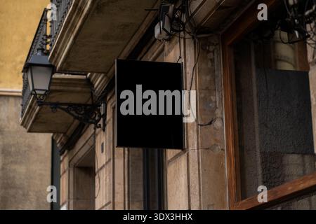 Blank black rectangular storefront sign mockup hanging on old stone building Stock Photo