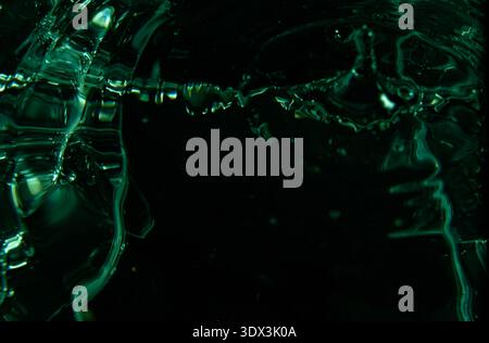 430.liquid surface, showing ripples and a splash. The image has a dark background with striking green and turquoise reflections abstract composition w Stock Photo