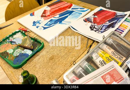 Close up of artwork creation featuring sketches of classic vintage mini cars and acrylic painting supplies on a wooden table Stock Photo