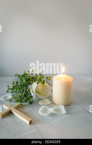 Minimal memorial arrangement with lit candle, white rose and wooden cross on marble, lots of copy space, faith and Holy Week concept. Stock Photo