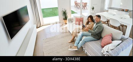 Happy mature old couple hugging sitting on sofa at home using digital tablet. Stock Photo