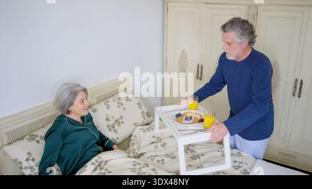 Husband bringing breakfast in bed to wife showing loving care Stock Photo