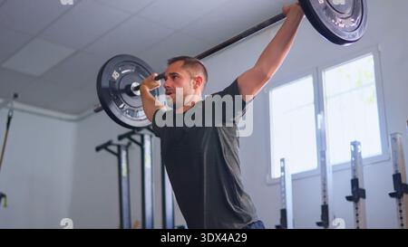 Man performing overhead press exercise with barbell in gym Stock Photo