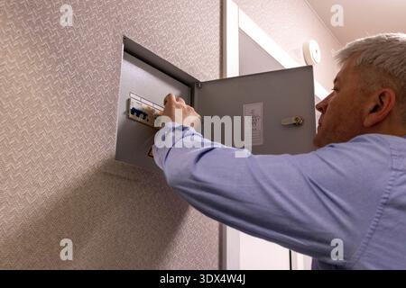 A man checks an indoor circuit breaker box Stock Photo