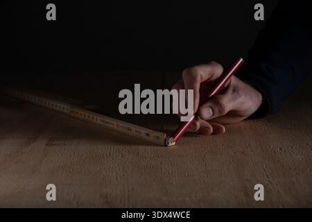 Close up of hand marking measurement with pencil using folding ruler on wooden floor. Concept of home renovation, carpentry work, accurate measuring a Stock Photo